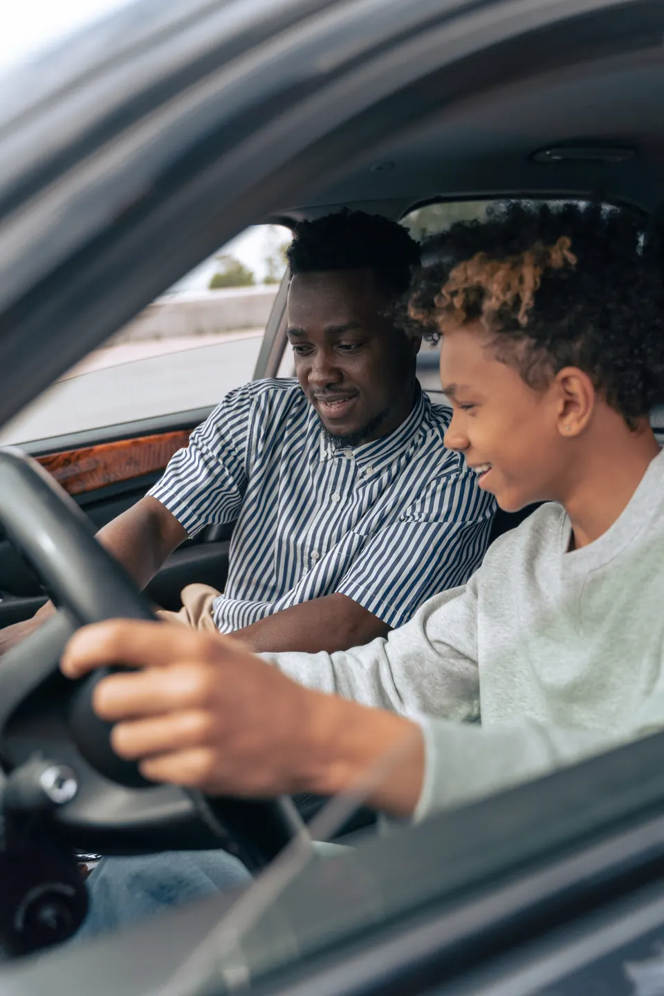 Smiling driving instructor teaching a teen student to drive during a behind-the-wheel lesson